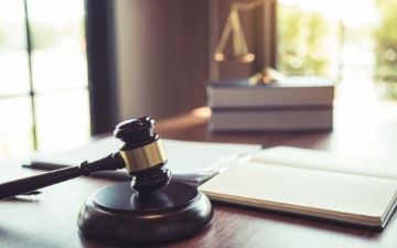 Wooden gavel and legal documents resting on a desk with the scales of justice in the background.