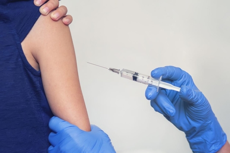 Person with blue gloves using syringe on woman's arm