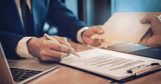 Attorney signing legal documents and handing an envelope to a client.