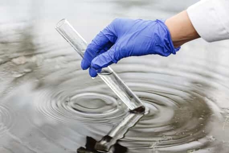 scientist with gloved hand tests water quality with test tube
